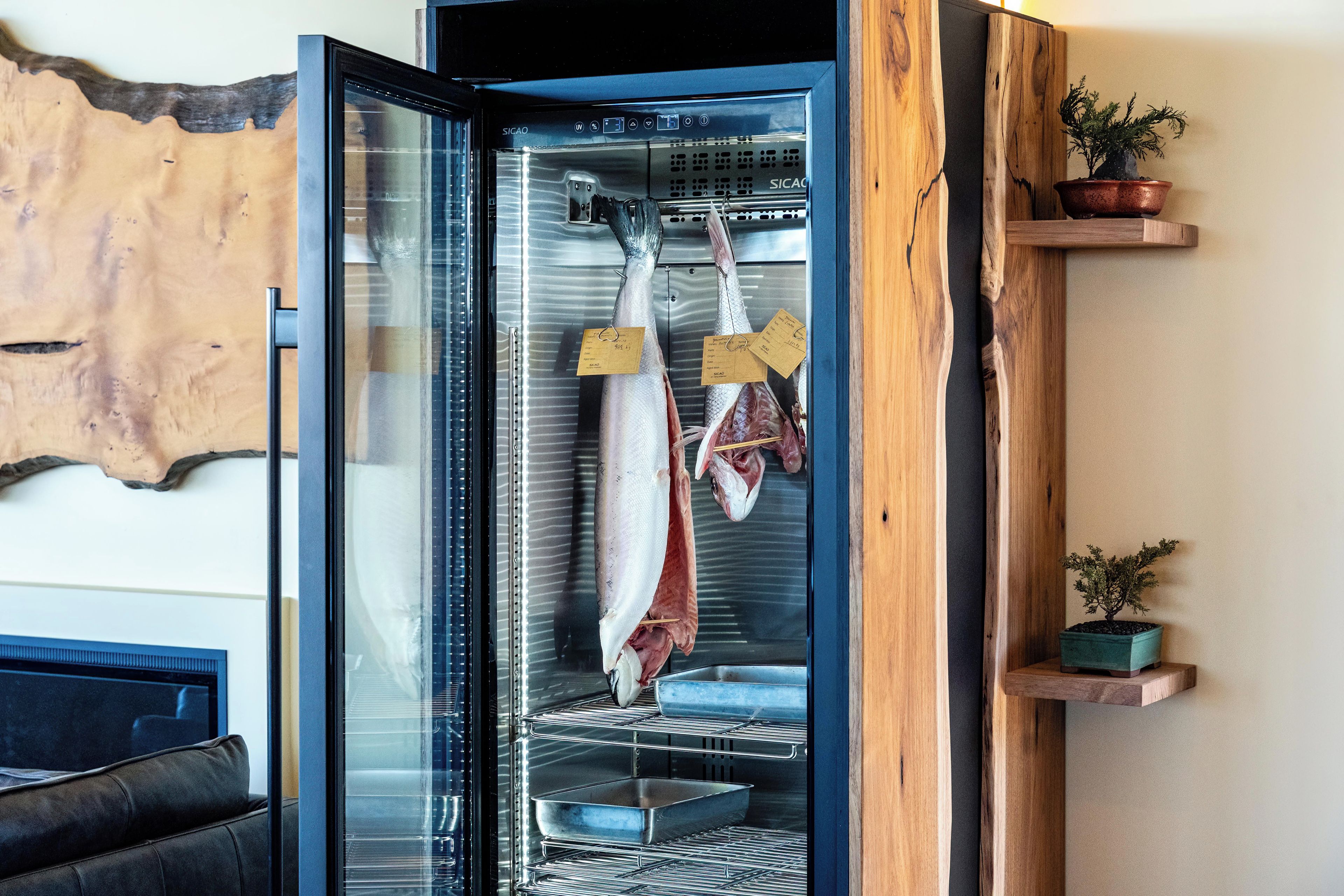 Una cocina moderna con refrigerador empotrado, estanterías de madera y una obra de arte original en la pared.