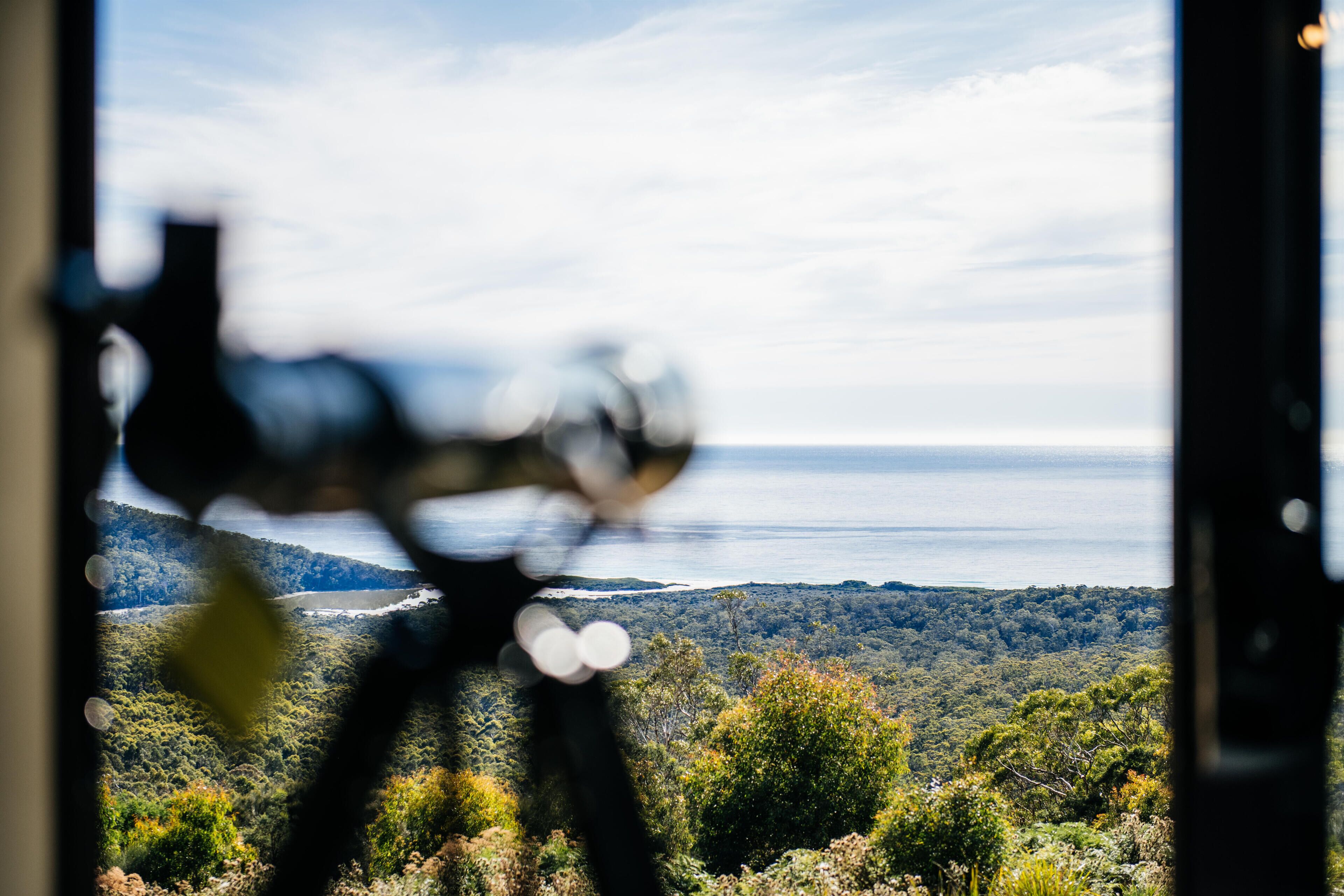 Vista a través de una ventana con un telescopio, que da al paisaje boscoso y a un cuerpo de agua.