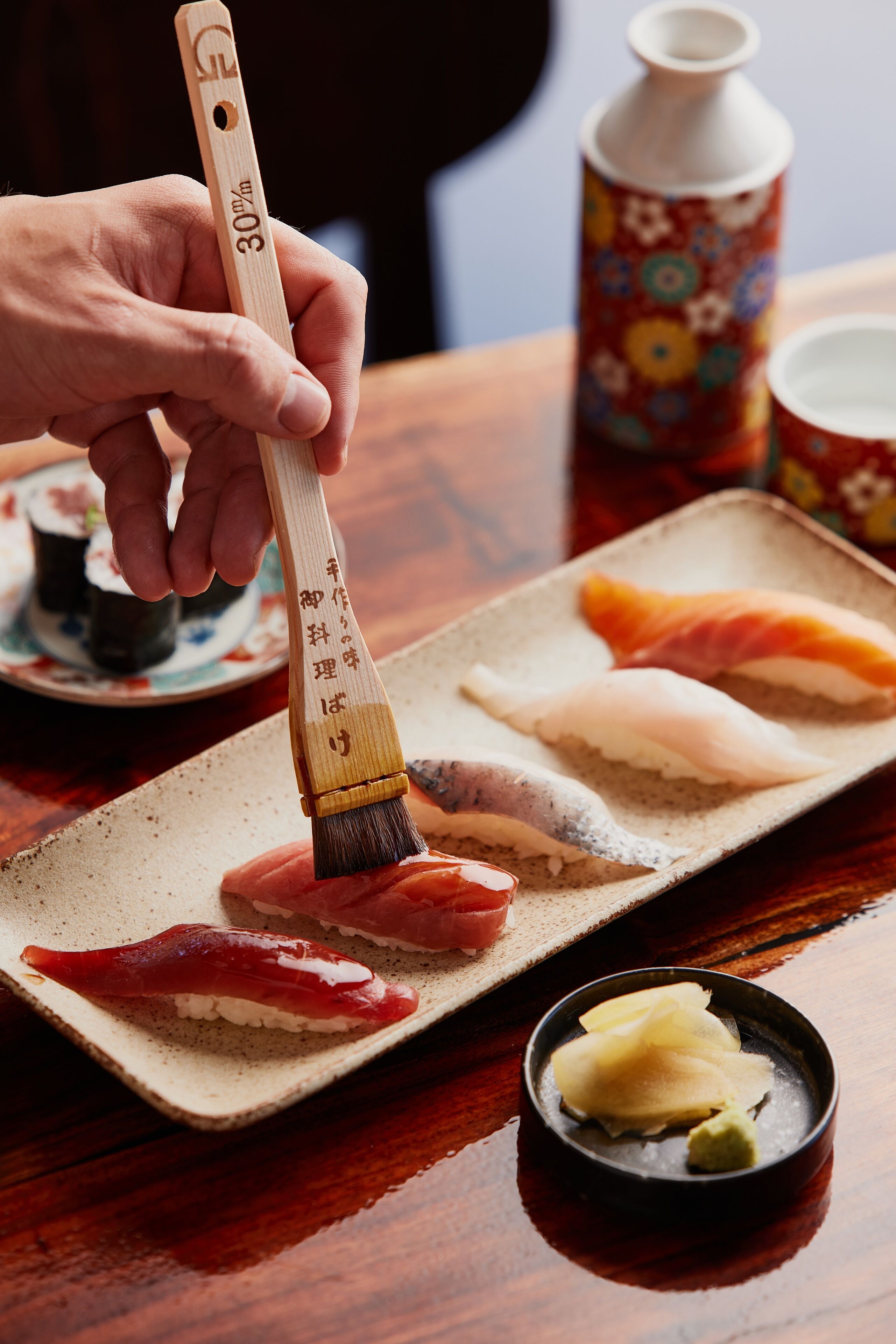 A person applying wasabi to sushi on a ceramic plate.