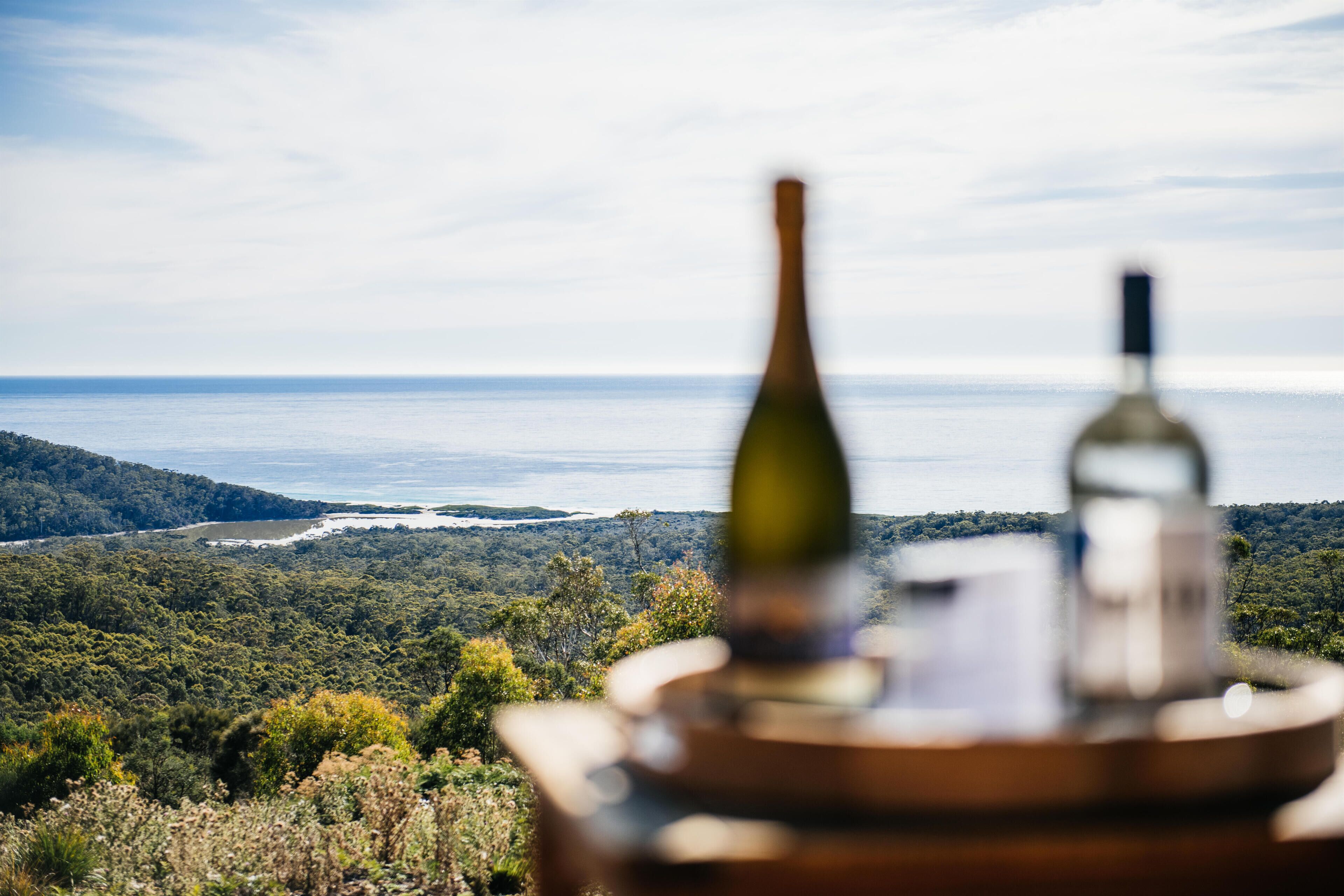 Vista de un paisaje costero, destacando una botella y un vaso sobre una mesa.