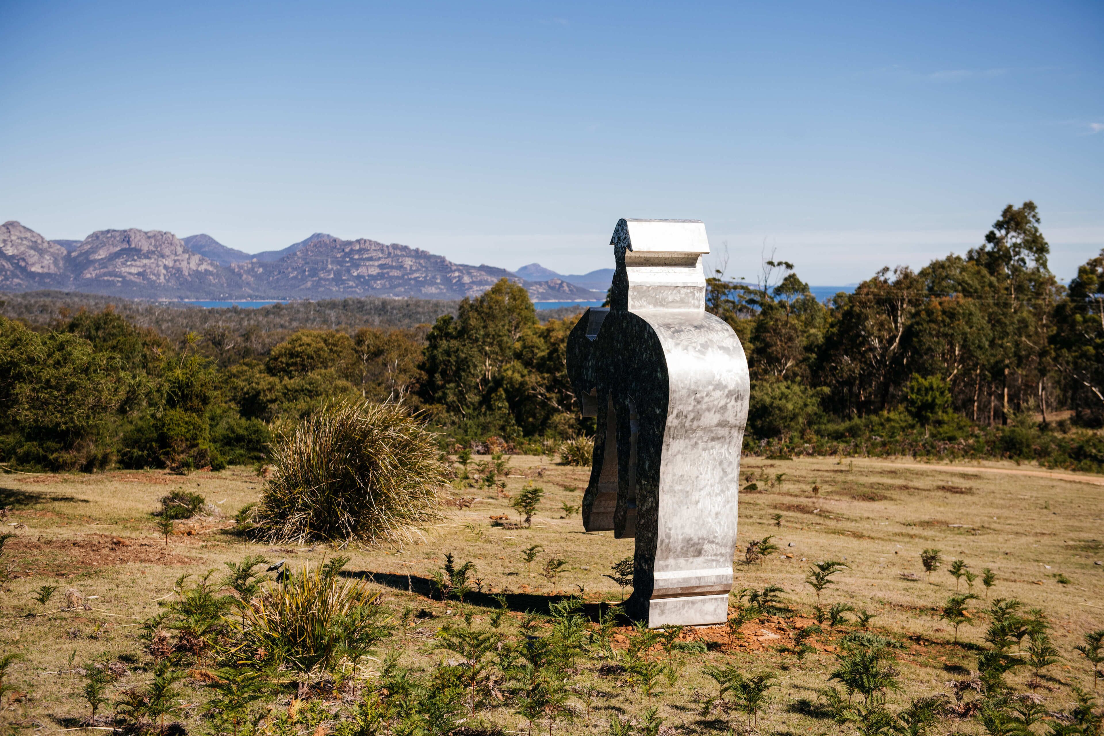 Un monument de pierre se dresse dans un champ verdoyant, avec une chaîne de montagnes en arrière-plan.
