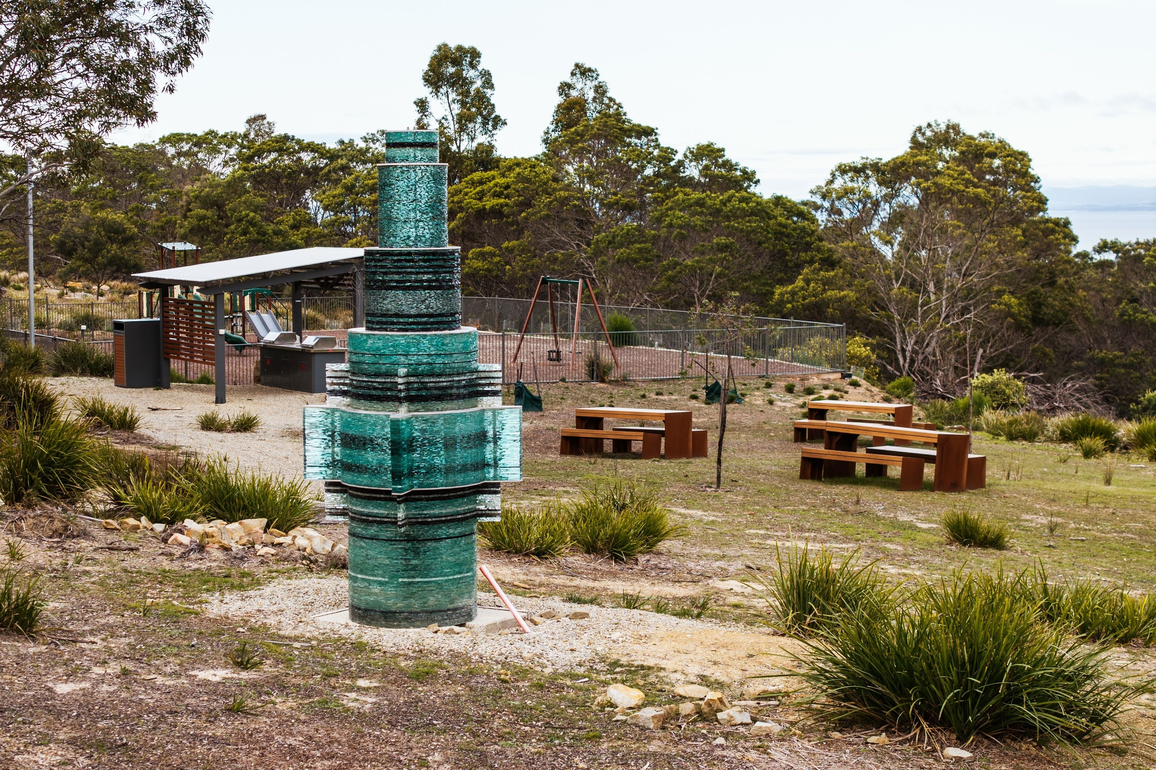 A park with a unique green sculpture, picnic tables, and a playground.