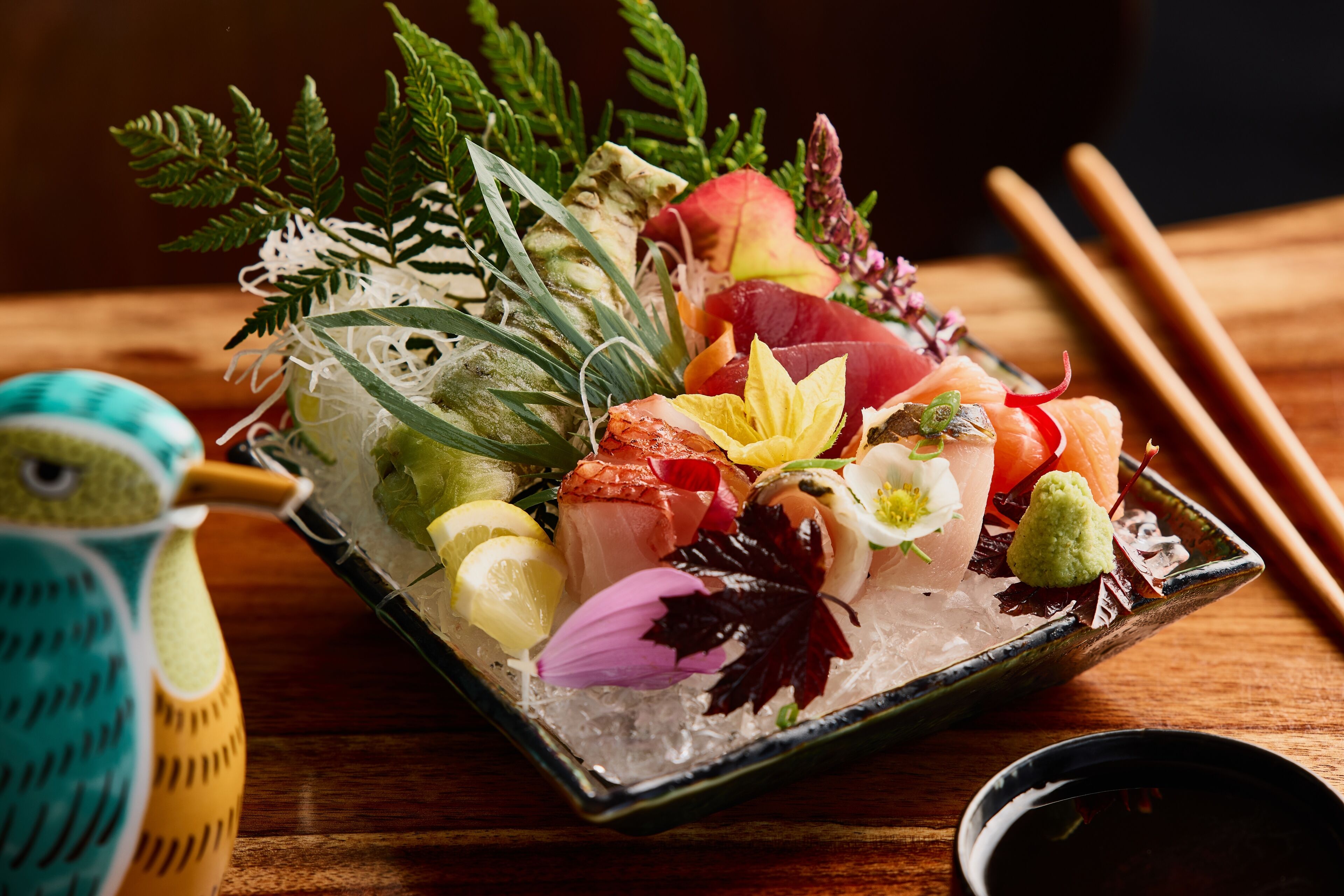 A sushi platter with various fish and garnishes on ice, accompanied by chopsticks and a small bowl of soy sauce.