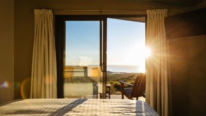 A bedroom with a bed, a chair, and a view of the ocean through a sliding door.
