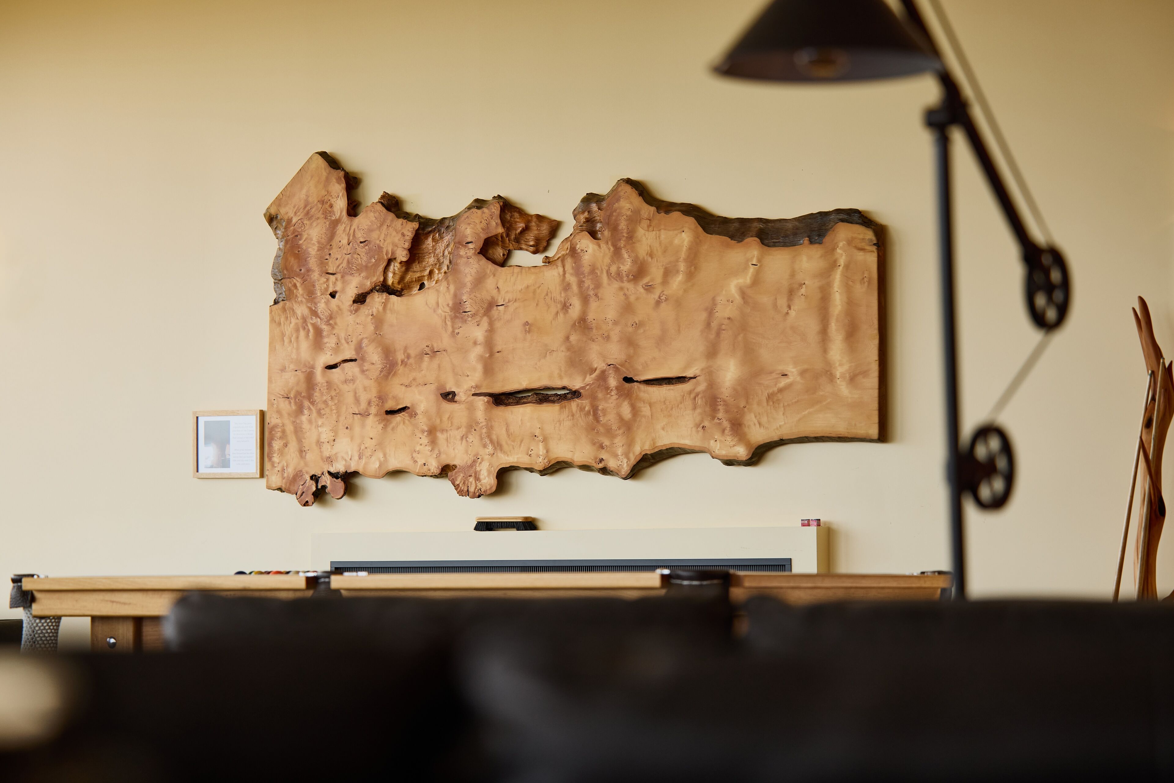 A room with a large wooden wall art piece, a desk with a computer, and a lamp.