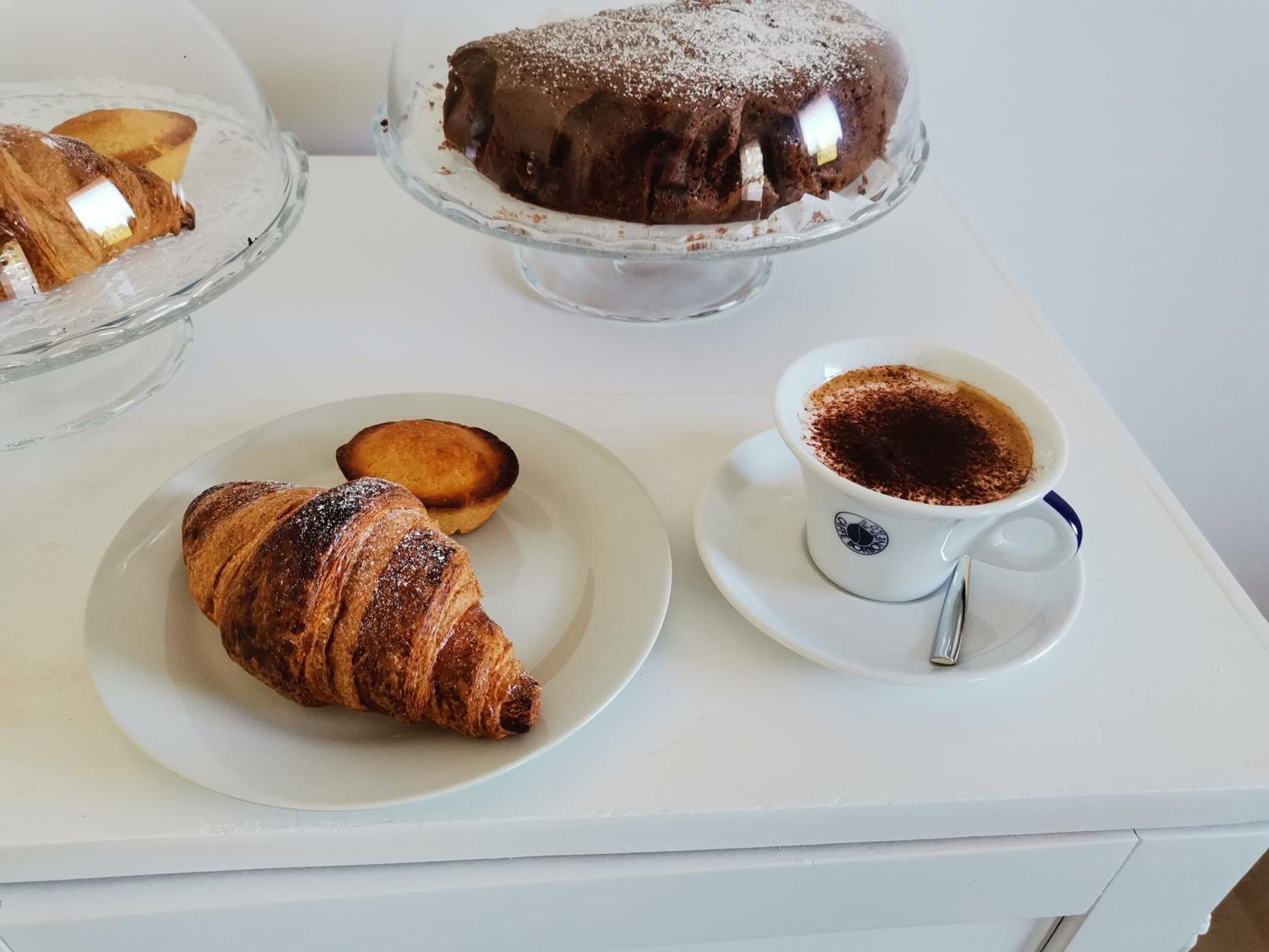 A dessert table with a chocolate bundt cake, a croissant, and a cup of coffee.
