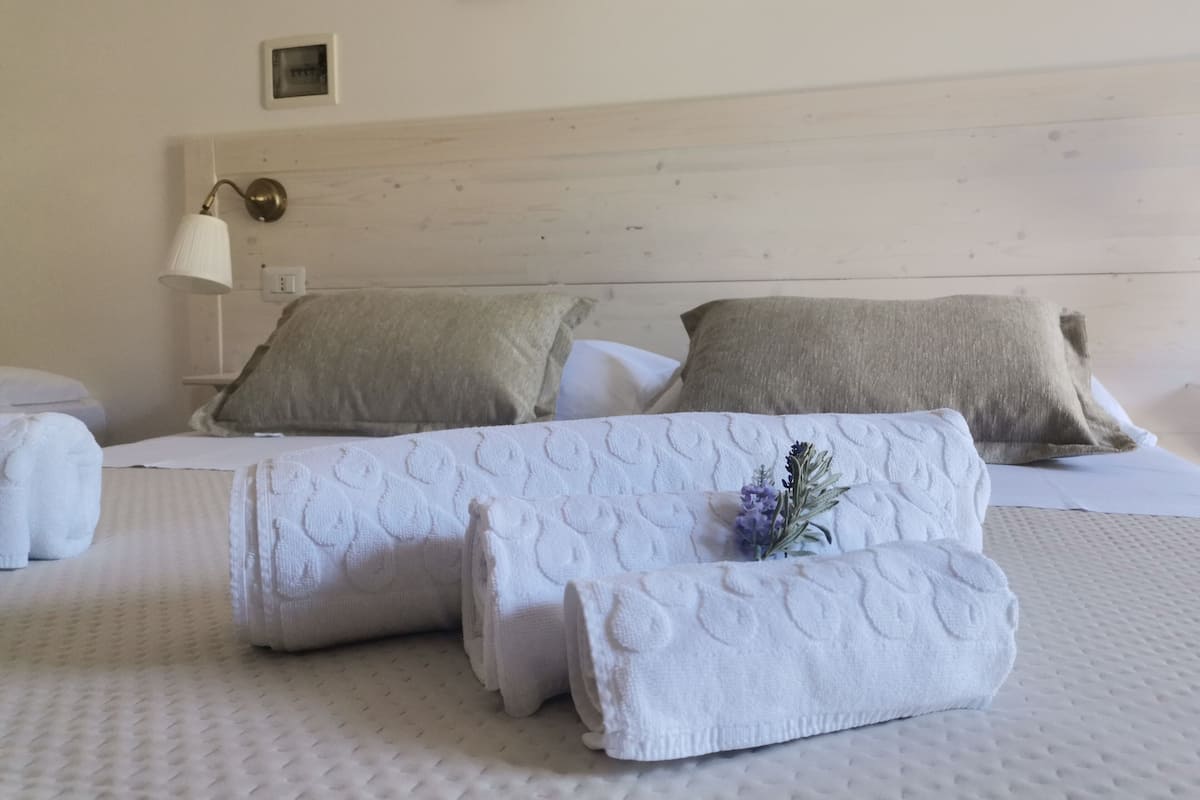 A neatly made bed with white linens and two pillows, a bedside lamp, and a small picture frame on the wall.