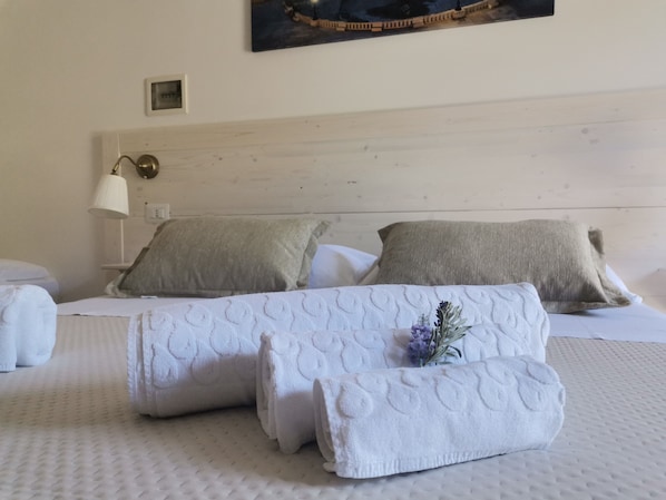 A neatly made bed with white linens and two pillows, a bedside lamp, and a small picture frame on the wall.