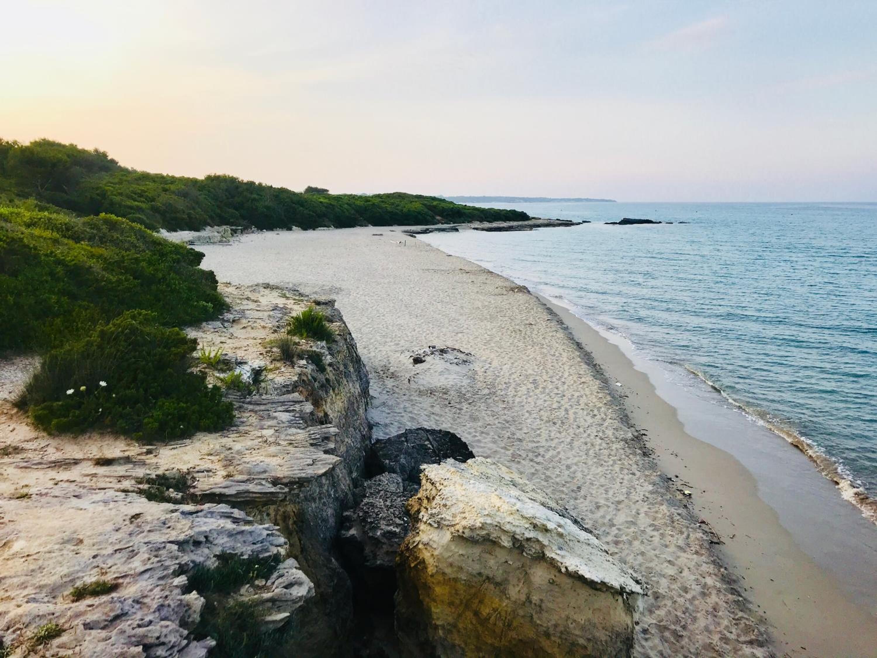 A coastal beach with a rocky shoreline and a clear view of the sea.