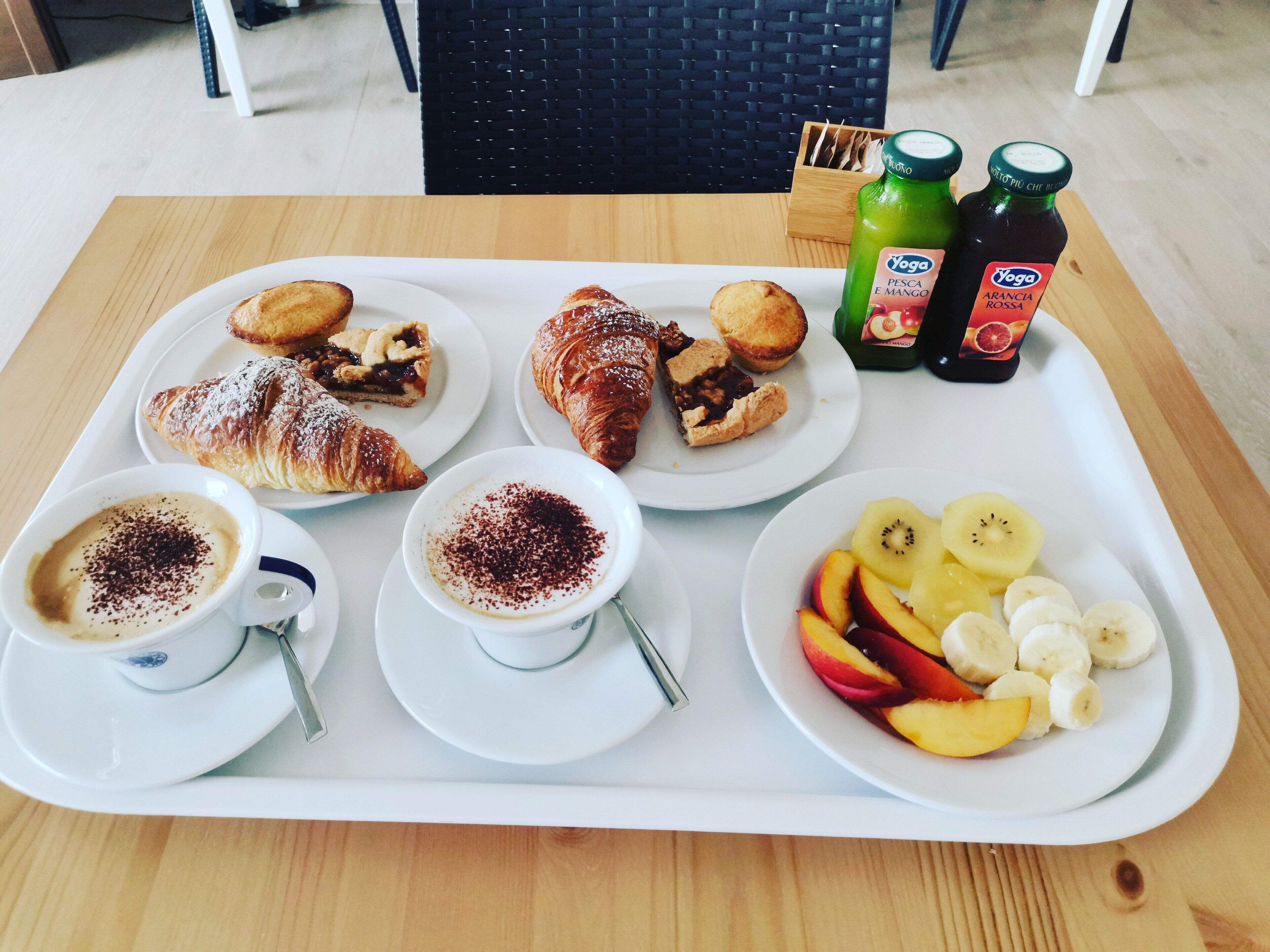 A tray with pastries, coffee, and fruit on a wooden table.