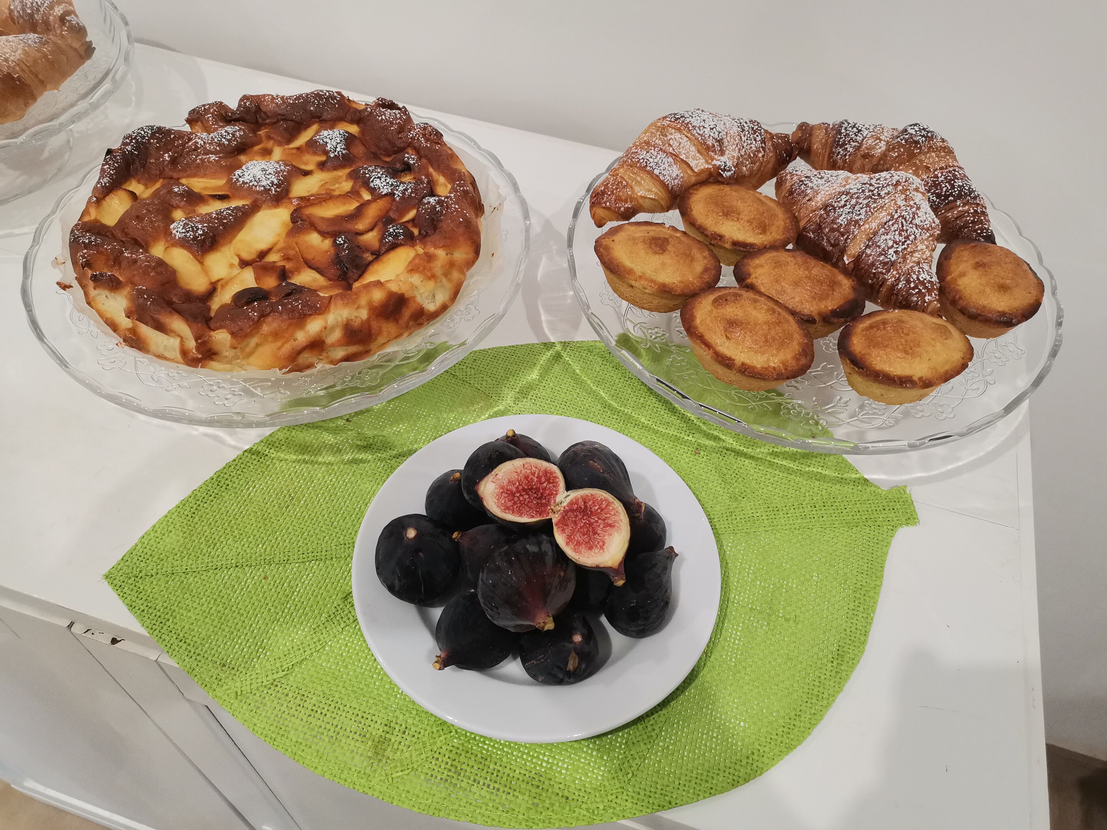 A table with three glass dishes containing baked goods and a plate of figs on a green placemat.