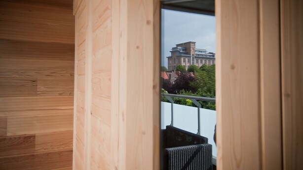 Un interior de madera con un amplio ventanal que muestra un edificio y follaje exterior.