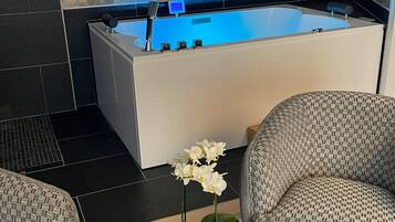 A modern bathroom with a large bathtub, a glass table with a potted orchid, and patterned chairs.