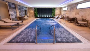 Una piscina interior moderna con sillas de descanso y un fondo de pared de piedra.