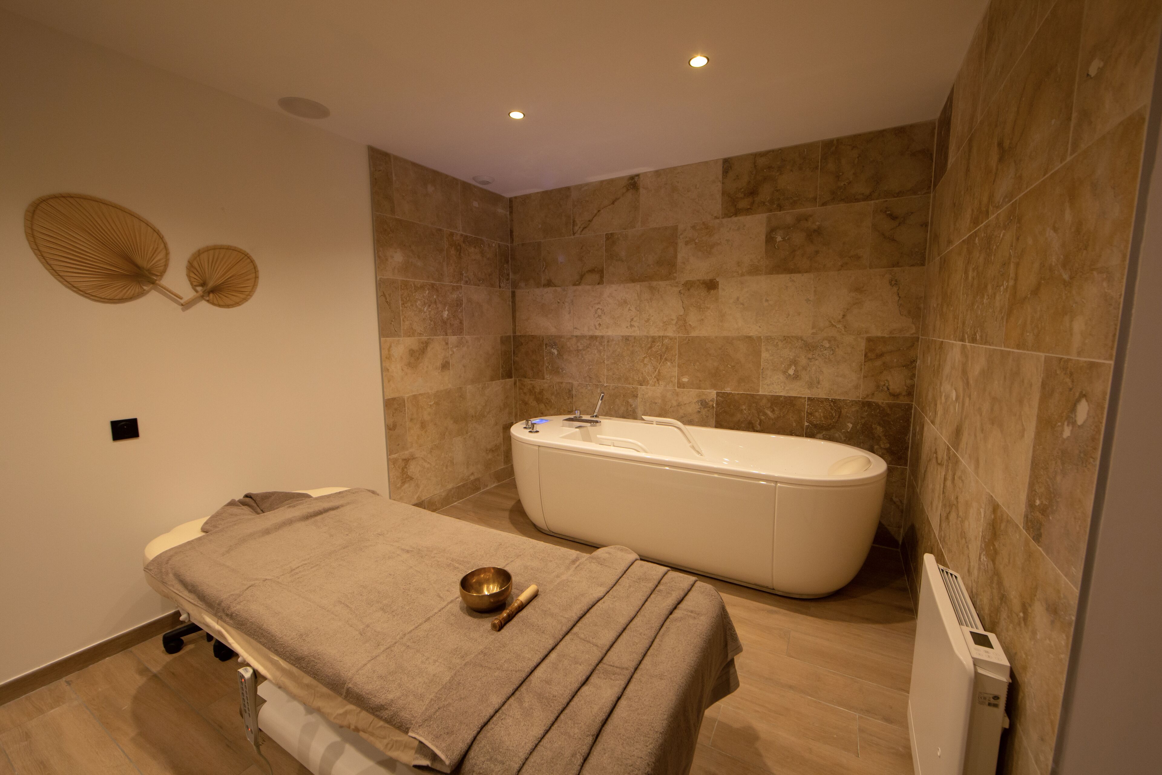 A modern bathroom with a freestanding bathtub, a massage table with a towel and a massage ball, and a wall-mounted fan.