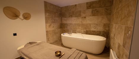 Un baño moderno con una bañera independiente, una mesa de masaje con una toalla y una pelota de masajes, y un ventilador fijado a la pared.