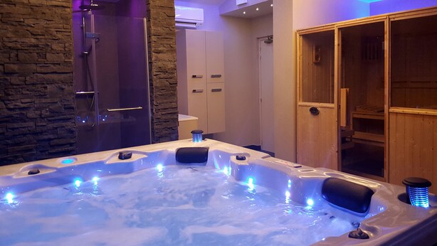 Un jacuzzi con luces LED azules, una pared de piedra, una puerta de madera y un mueble de madera.