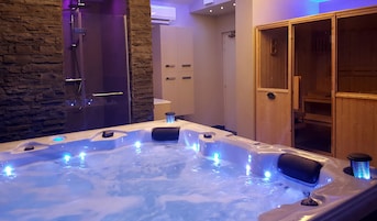 Un jacuzzi con luces LED azules, una pared de piedra, una puerta de madera y un mueble de madera.