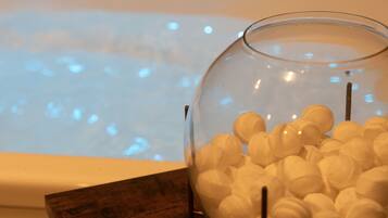 A glass bowl filled with white objects on a wooden surface next to a bathtub with a lighted background.