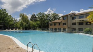 Ein klarer Swimmingpool mit Liegestühlen und ein Gebäude mit vielen Fenstern im Hintergrund.
