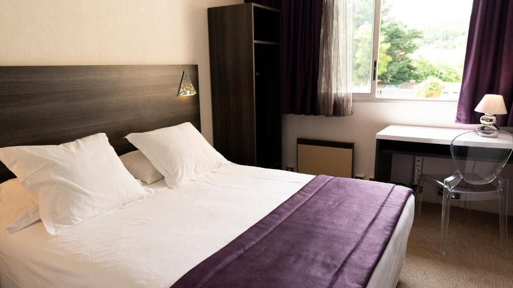 Una habitación de hotel con una cama grande, un escritorio, una silla y un ventanal con cortinas.