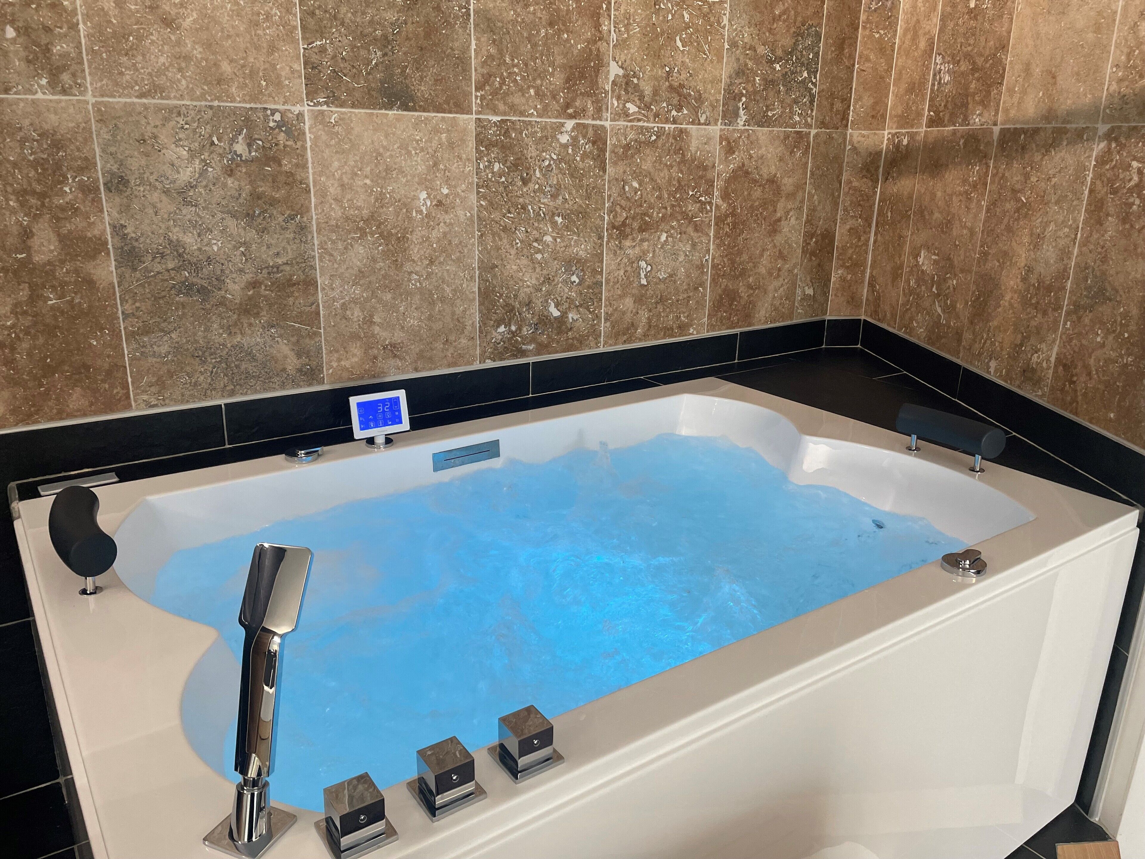 A modern bathroom with a large bathtub, a digital thermometer, and a handheld showerhead.