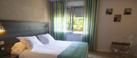 Una habitación de hotel con una cama, una mesita de noche, una silla y un ventanal con cortinas.