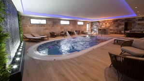 Un área interior de piscina moderna con pared de piedra, sillones de descanso y zona de bar.