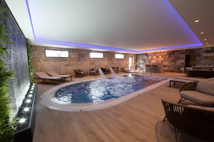 Un área interior de piscina moderna con pared de piedra, sillones de descanso y zona de bar.