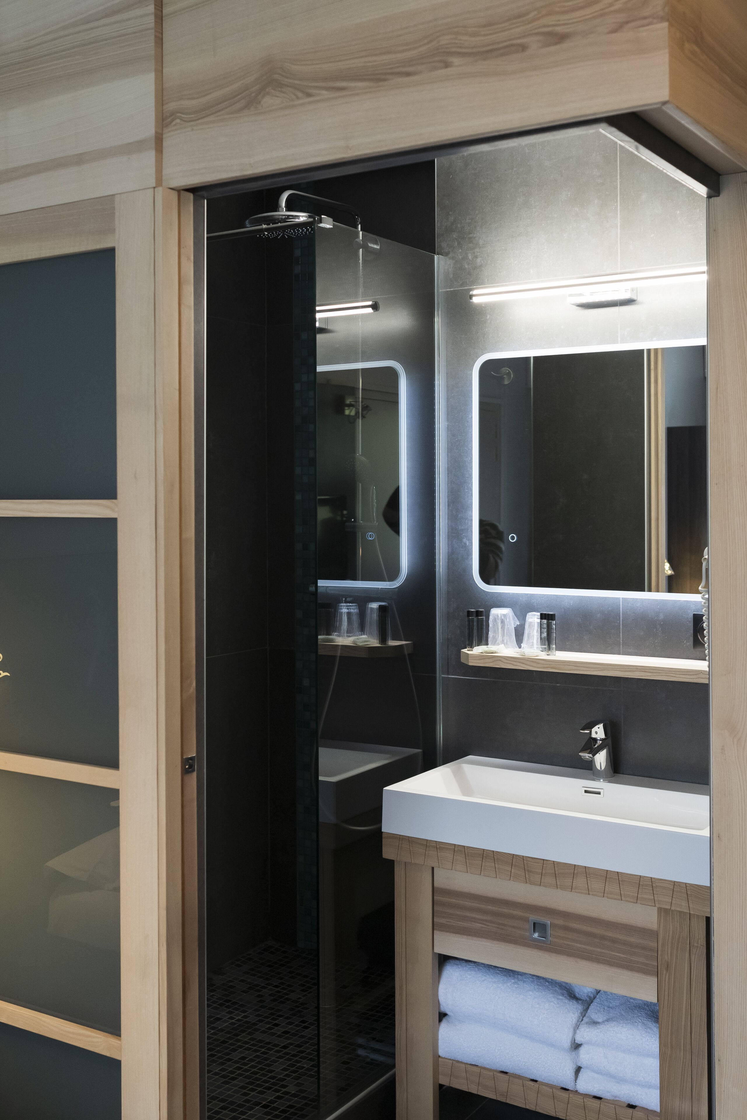 A modern bathroom with a glass shower enclosure, a large mirror, and a vanity with a sink and towel storage.