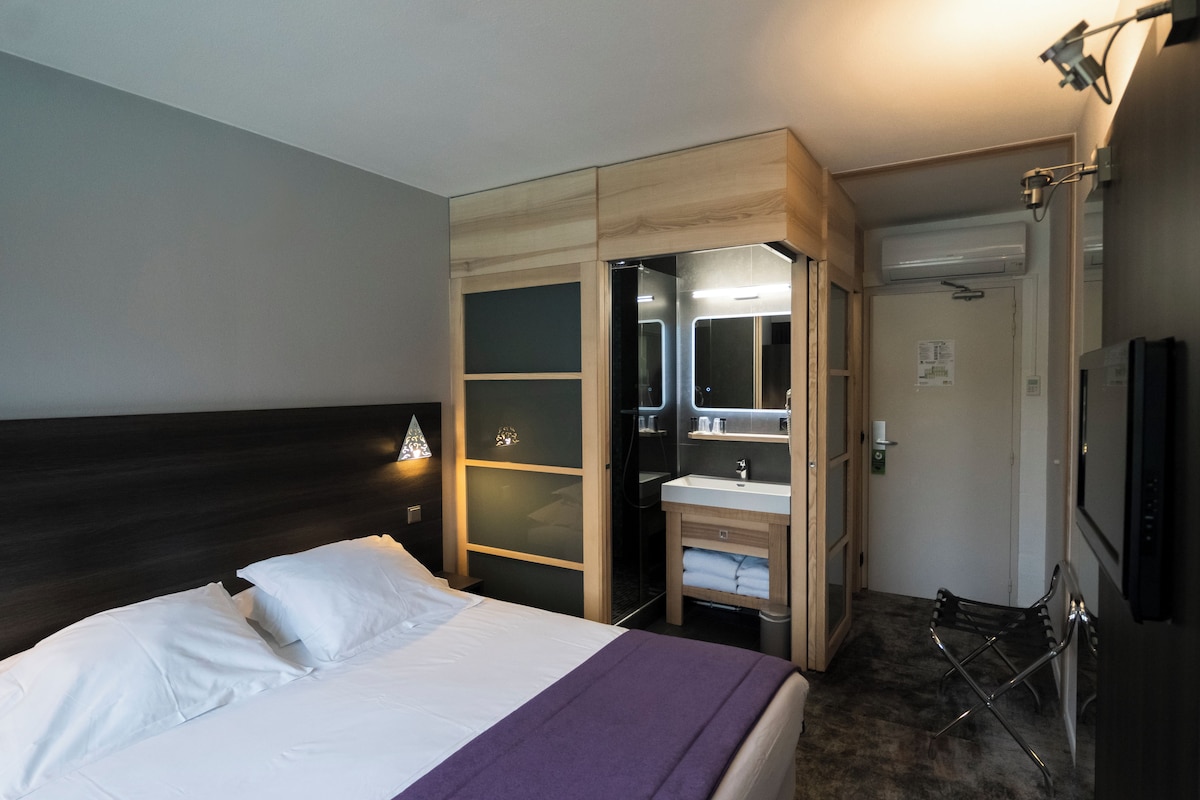 A hotel room with a bed, a bathroom with a mirror, and a shower.