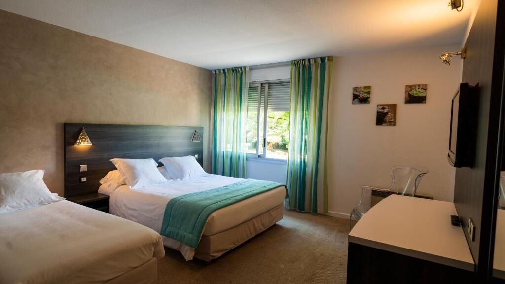 A hotel room with two beds, a desk, a chair, and a window with curtains.