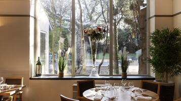 Un comedor con una mesa redonda dispuesta para cuatro personas, un florero con flores y una botella de vino en el alféizar de la ventana.