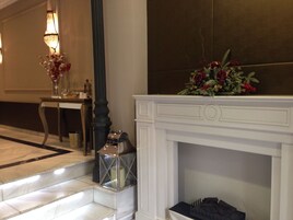 Un vestíbulo de hotel con una chimenea blanca, una mesa con un florero y un farol decorativo.