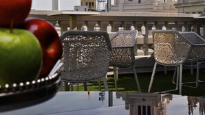 A view of a historic building with a clock tower, a reflection on a water surface, and a table with fruit and chairs. - Boutike Cibeles (Madrid)