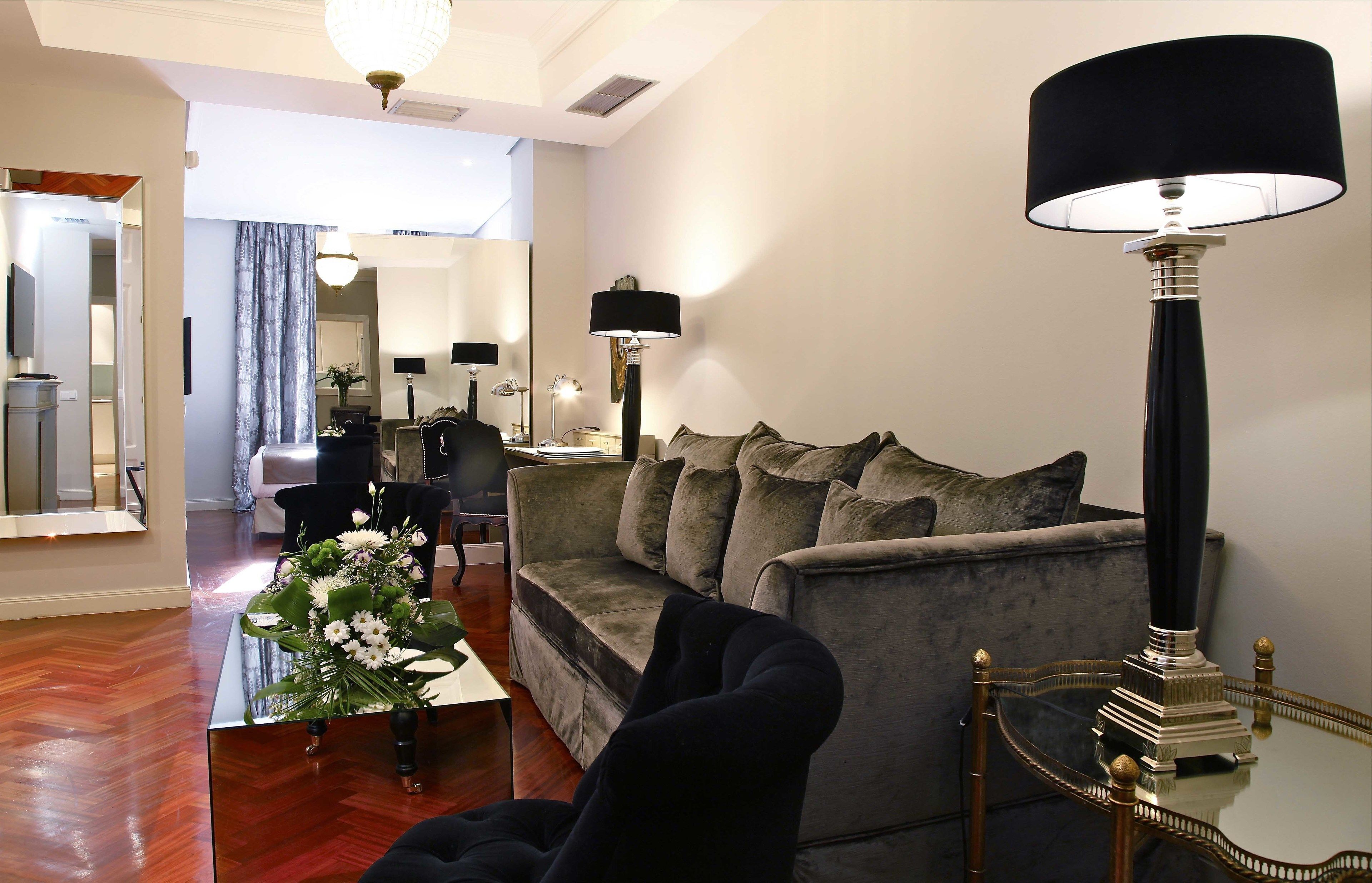 A modern living room with a grey sofa, a black armchair, a glass coffee table with a floral centerpiece, and a tall floor lamp.