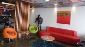A modern lobby with a red sofa, a green chair, and a wooden partition. - Hotel El Conquistador (Cuenca)