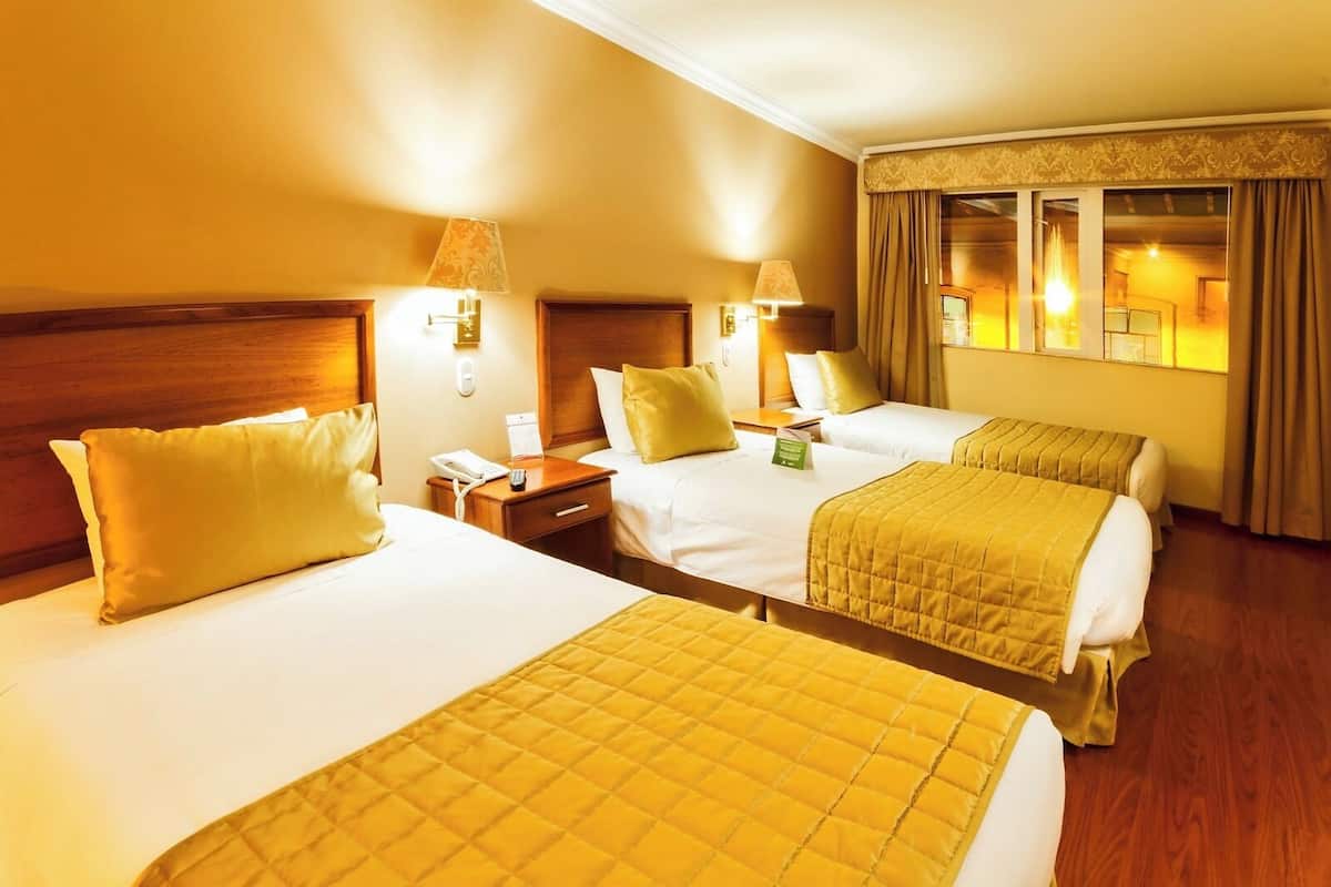 Habitación de hotel con dos camas, cabeceros de madera, lámparas de noche y una ventana con cortinas.