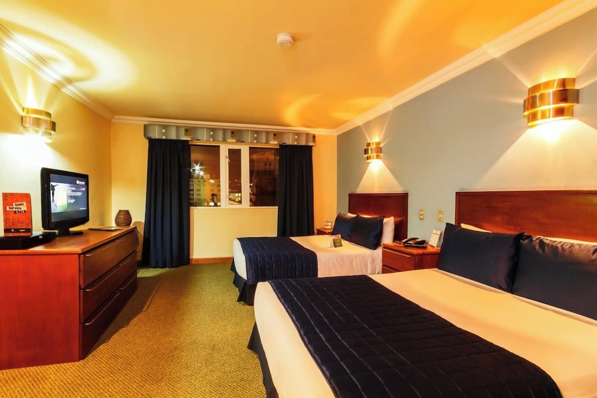 Habitación de hotel con dos camas, un escritorio con televisor y una ventana con cortinas.