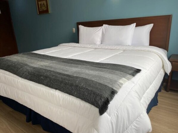 Cama bem arrumada com roupa de cama branca e manta listrada em cinza e preto.