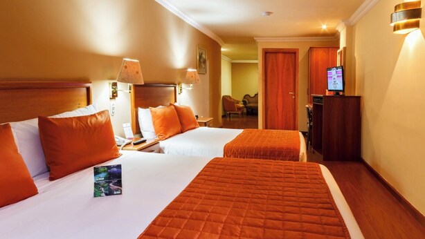 A hotel room with two beds, a TV, and a desk with a lamp. - Hotel El Conquistador (Cuenca)