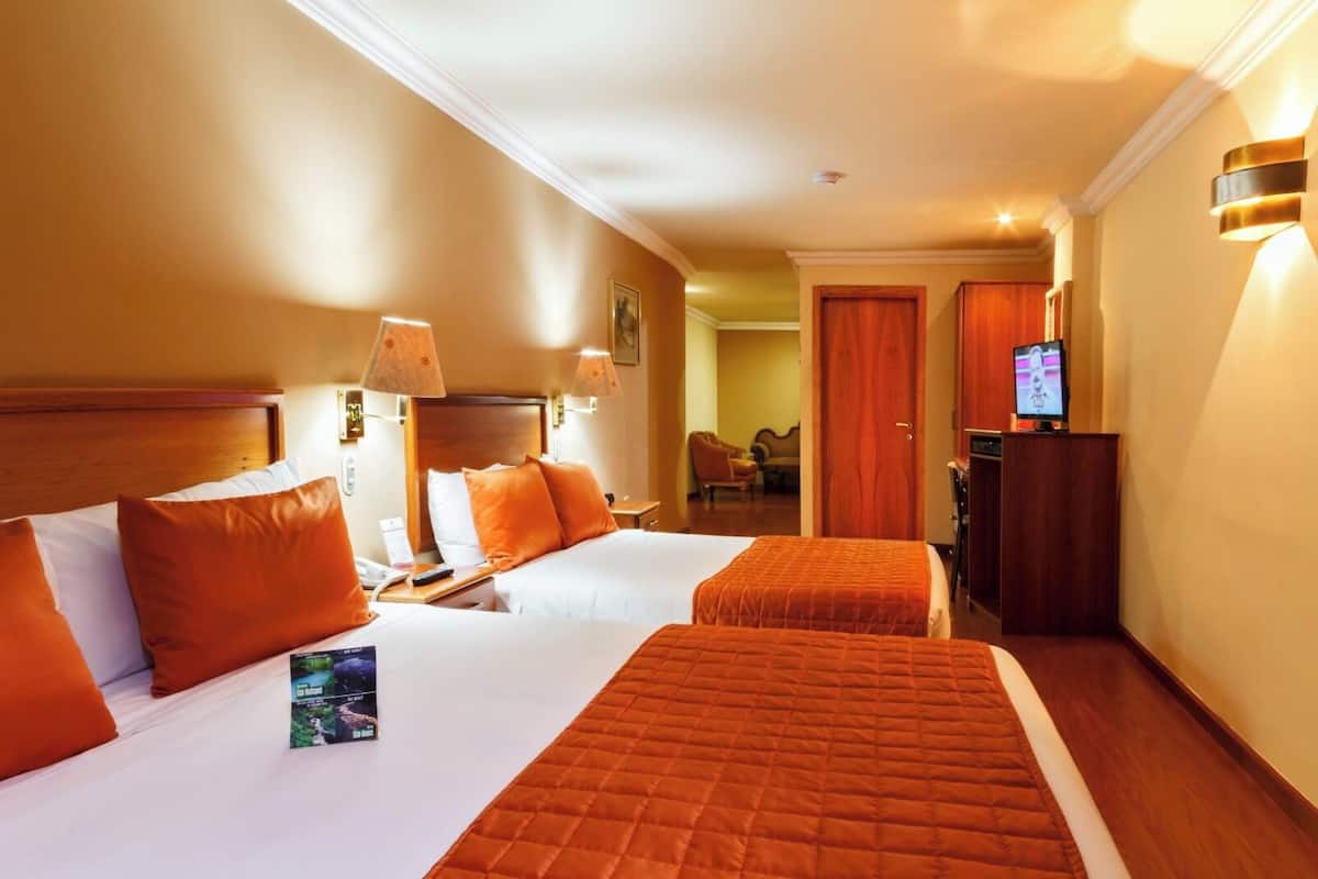Habitación de hotel con dos camas, un televisor y un escritorio con lámpara.