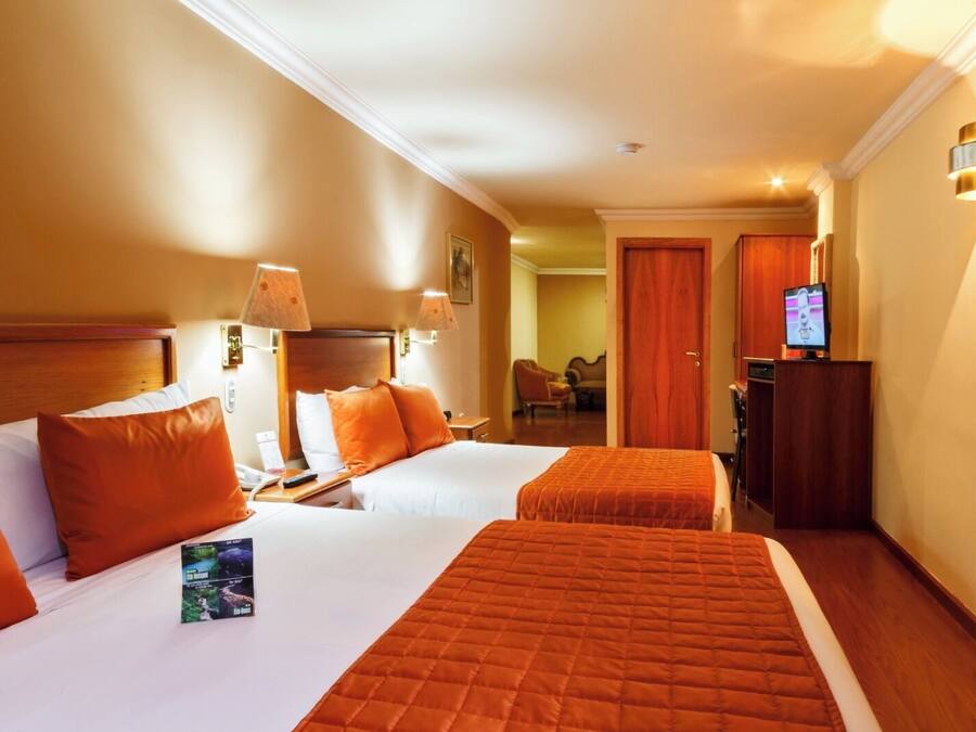 Habitación de hotel con dos camas, un televisor y un escritorio con lámpara.