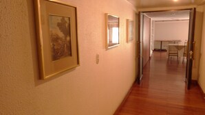A hallway with framed artwork on the wall, a wooden floor, and a dining area in the distance. - Hotel El Conquistador (Cuenca)