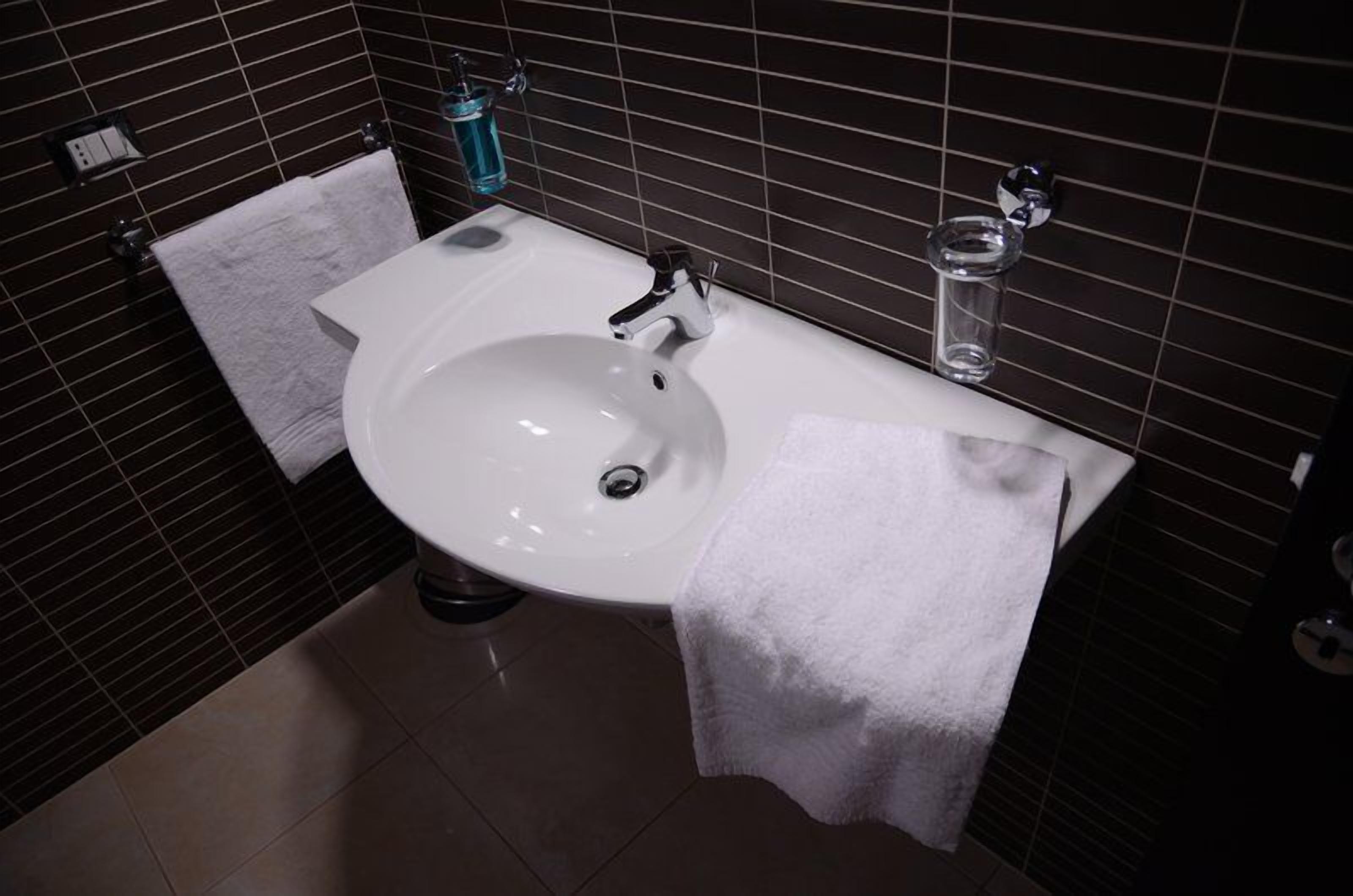A bathroom with a white sink, a towel, and a glass of water on the counter.