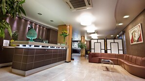 Un hall d’hôtel moderne comprenant un comptoir d’accueil, un espace salon et des plantes décoratives.