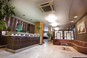 Una moderna hall d'albergo con reception, area salotto e piante ornamentali.