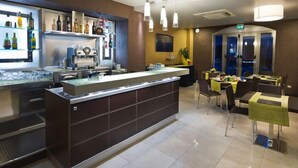 Un espace bar moderne comprenant un comptoir, des étagères remplies de bouteilles et un coin repas avec des tables et des chaises.