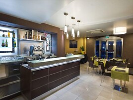 Una zona bar moderna con un bancone, scaffali pieni di bottiglie e un'area ristorazione con tavoli e sedie.