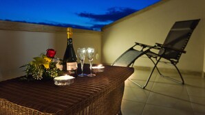 Une table en osier, agrémentée d’une bouteille, de verres et d’une bougie, avec une chaise et une vue sur le ciel.